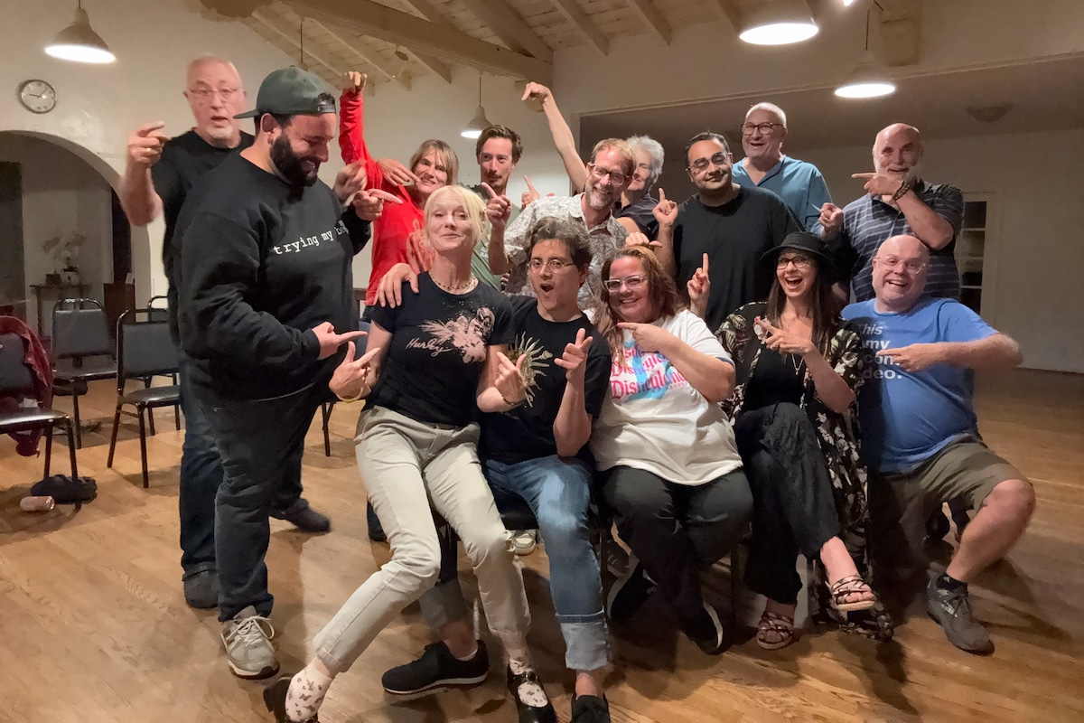 A lively group of people posing together in a room, playfully pointing at each other with smiles and expressions of joy.